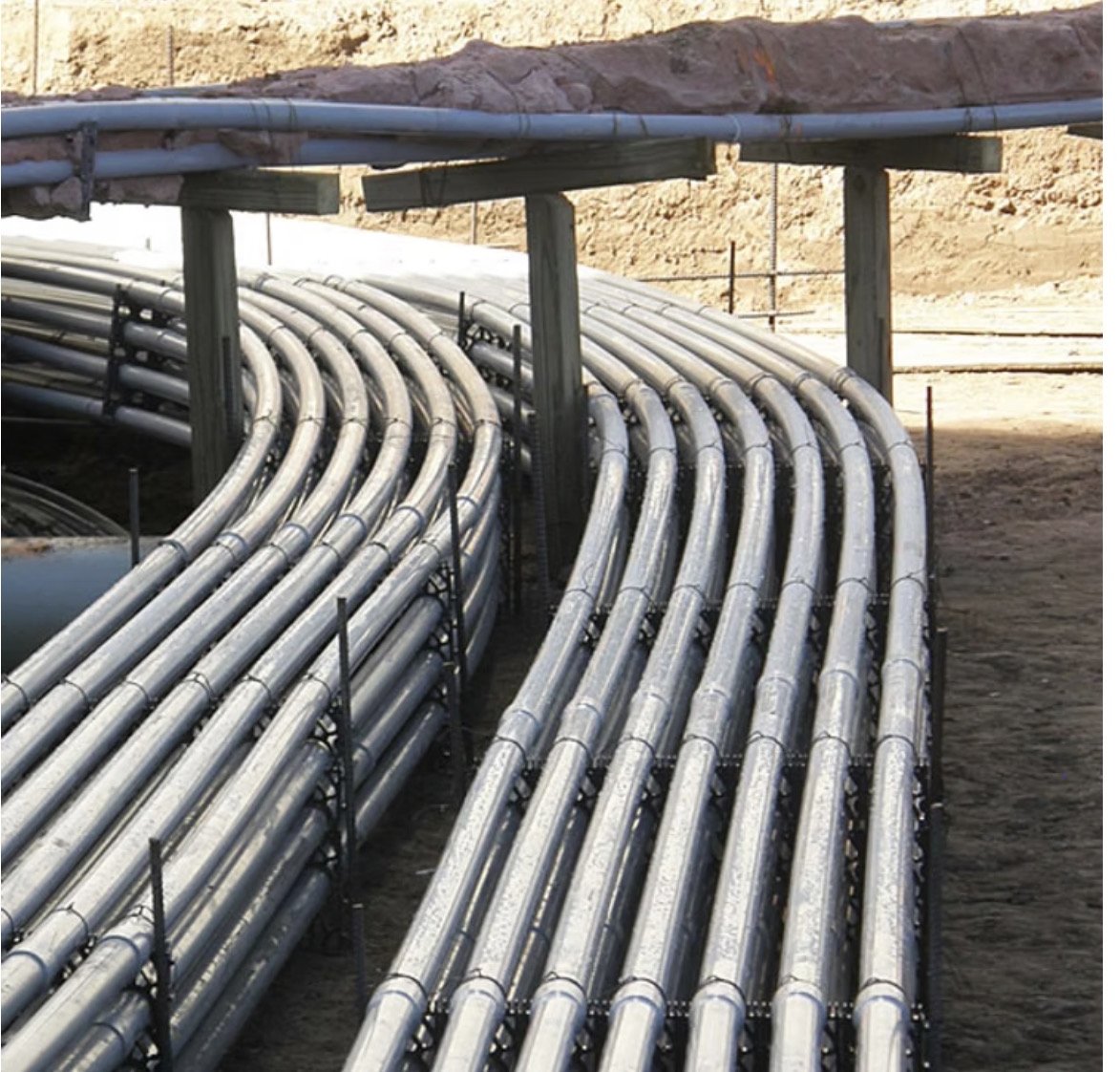 A bank of curved steel conduit runs set in an excavated trench